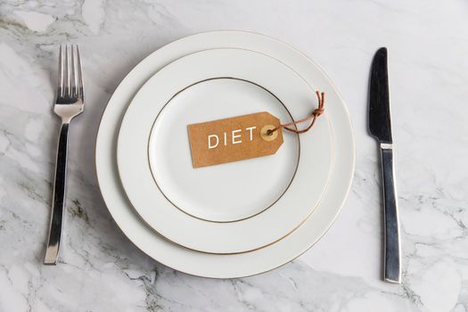 Serving two plates, spoon, fork, knife on the marble table. The concept of weight loss and diet. The concept of weight loss and diet. Label with the inscription - diet in an empty plate