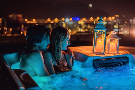 Portrait of young carefree happy smiling couple relaxing at hot tub during enjoying happy traveling moment vacation. Life against the background of green big mountains at night.