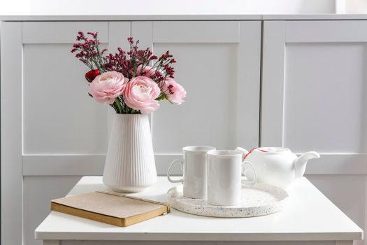 Bouquet of pink Persian buttercups on a white table in front of a chest of drawers. Scandinavian style. Place for text