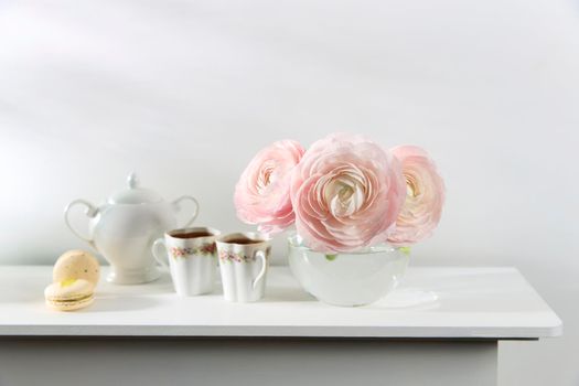 Three pale pink ranunculus in a transparent round vase on the white windowsill. Copy space. Place for text