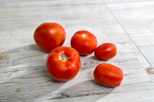 Different types of fresh tomatoes lie on a beige wooden table