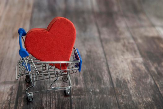 A supermarket trolley with the big paper heart, home delivery of love are on the brown wooden background. Copy space