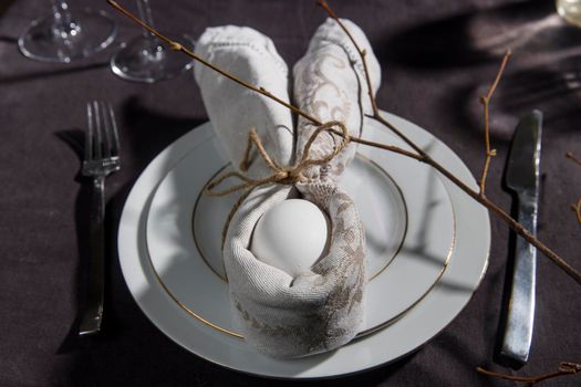 Napkin folder idea. Easter table. Easter holiday table setting with egg in grey napkin Easter Bunny on a brown linen background. Copy space, top view, flat lay.