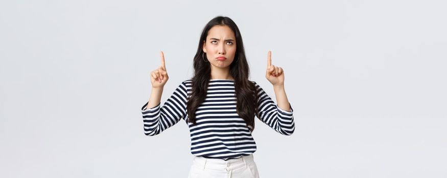 Lifestyle, beauty and fashion, people emotions concept. Skeptical and disappointed moody asian girlfriend complaining, pouting unsatisfied and pointing fingers up.