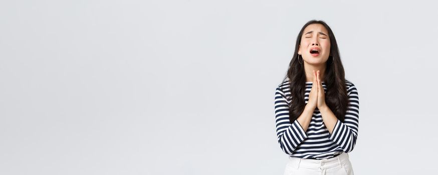 Lifestyle, people emotions and casual concept. Desperate hopeful asian girl making wish, close eyes and hold hands in pray, pleading god to have something, making wishful face, white background.
