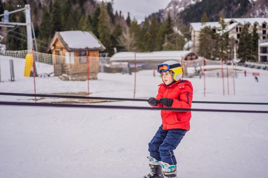 Boy uses a training lift. Child skiing in mountains. Active toddler kid with safety helmet, goggles and poles. Ski race for young children. Winter sport for family. Kids ski lesson in alpine school. Little skier racing in snow.