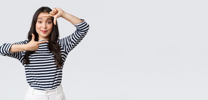 Lifestyle, people emotions and casual concept. Creative cute asian girl picturing, capture moment with hand frames gesture, smiling amused, staying positive and happy, white background.