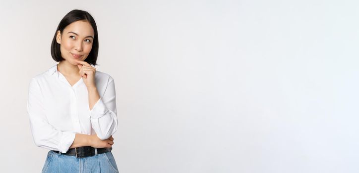 Image of thoughtful smiling woman has an idea, scheming, planning, looking aside and thinking, standing in office white blouse against studio background.