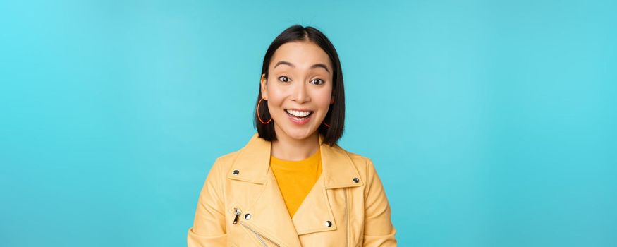 Close up portrait of asian girl looks surprised at amazed, wow face expression, stands over blue background.