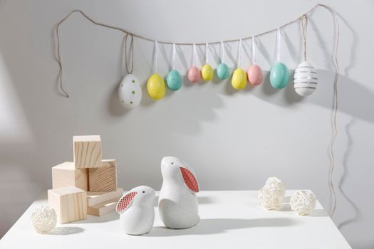 Fragment of the interior. Decorated children's room for Easter. A garland of plastic eggs on the wall. Ceramic rabbits and wooden cubes on the table. Place for your text. Easter card.