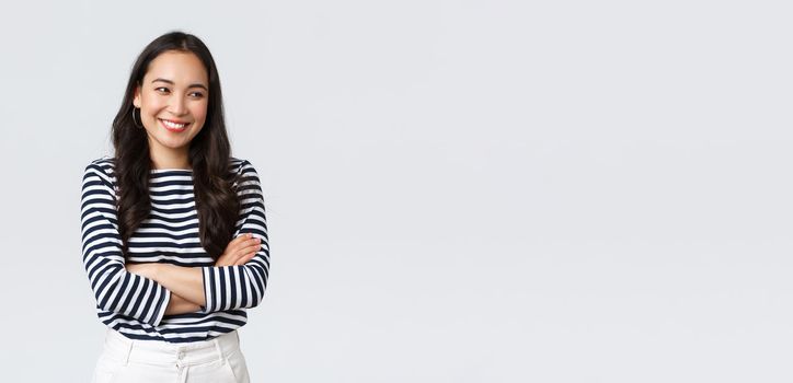 Lifestyle, beauty and fashion, people emotions concept. Cheerful cute and shy asian girl cross arms chest modest pose, looking away as laughing and smiling silly, stand white background.