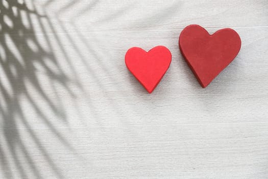 Two paper hearts and a shadow from a palm branch are on the tiled beige tiles. Space for text. Copy space.