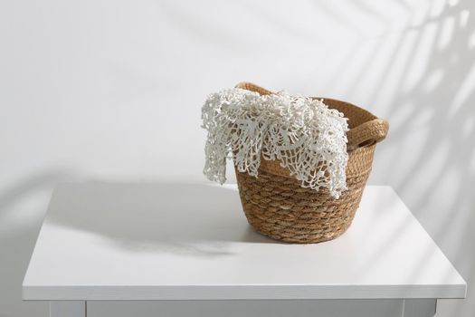 A wicker basket with lace on a chest of drawers. The shadow of a palm leaf. Place for text