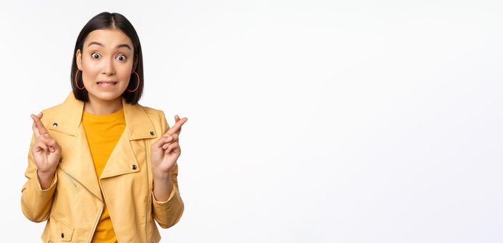 Portrait of excited asian woman looks hopeful, wishing, praying or begging, waiting for news, standing over white background, smiling enthusiastic.