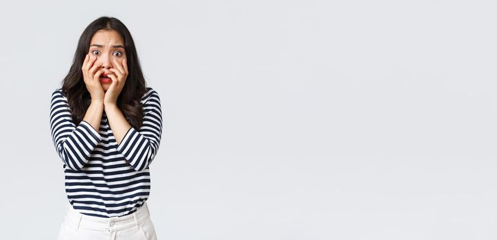 Lifestyle, people emotions and casual concept. Scared timid and insecure woman hold hands near mouth, screaming and looking terrified, shivering from fear, stand white background.