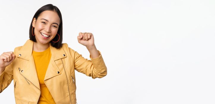 Image of asian woman dancing and smiling happy, celebrating victory, triumphing, standing over white background. copy space
