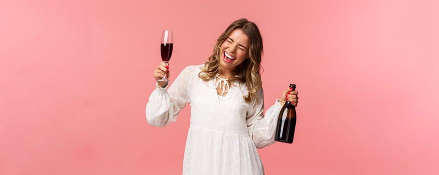 Holidays, spring and party concept. Portrait of excited and emotive good-looking blond girl dancing and celebrating, having fun saying yeah singing closed eyes, hold glass wine and bottle.