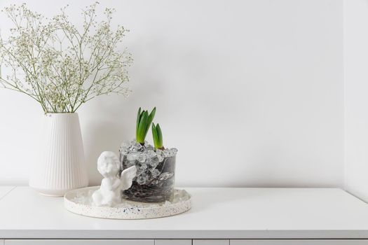 Gypsophila in a ceramic vase, hyacinths in a glass vase on a white dresser. View of modern scandinavian style interior. Living room, commode with vases. Minimalism concept