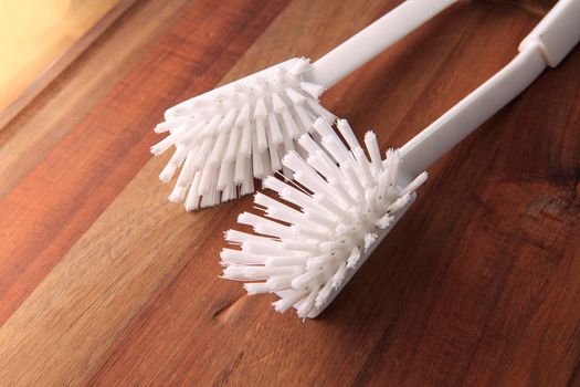 Two white plastic dishwashing brushes on a wooden table surface