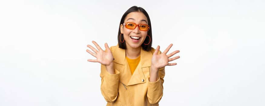 Surprised jazz hands. Happy asian girl smiling, looking amazed at camera, announcing smth, standing over white background.
