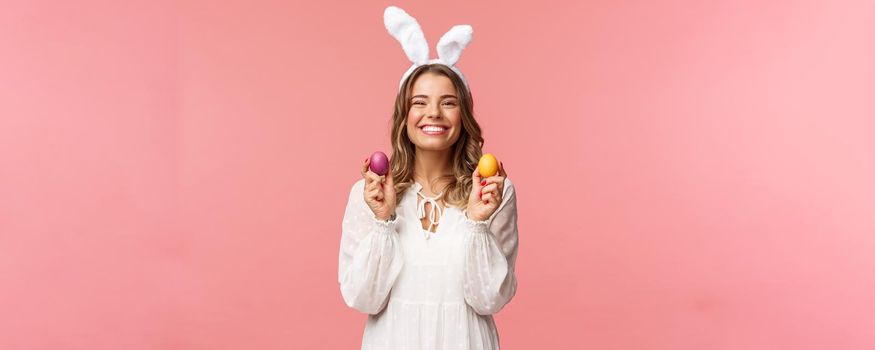 Holidays, spring and party concept. Portrait of lovely, cheerful blond girl in rabbit ears, holding colored eggs, celebrating Easter with family, enjoying spend traditional day with close people.