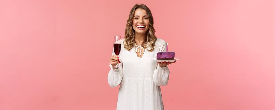 Holidays, spring and party concept. Portrait of excited good-looking young tender girl celebrating birthday, having fun with friends, eating b-day cake and drink wine from glass, laughing joyfully.
