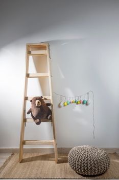 Fragment of the interior of the children's room, decorated for Easter. A ladder with a bear, a garland of fake colored eggs. Easter card