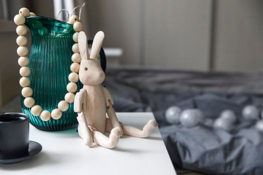 A heavy green glass jug, a wooden hinged rabbit and a cup of coffee are on the bedside table