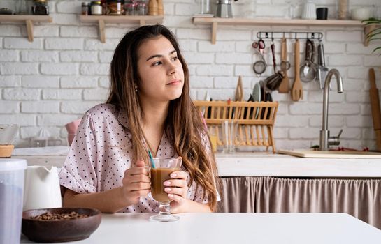 Alternative coffee brewing. young woman in lovely pajamas drinking coffee with milk at home kitchen