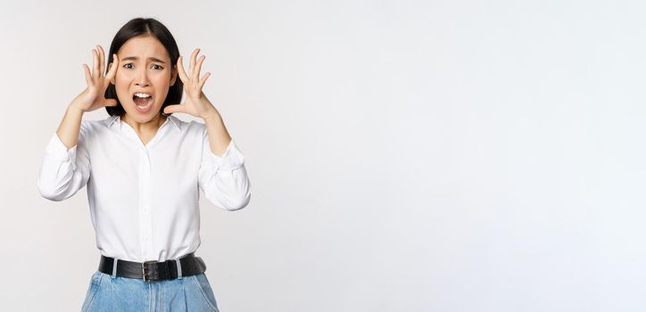 Image of shocked anxious asian woman in panic, holding hands on head and worrying, standing frustrated and scared against white background.