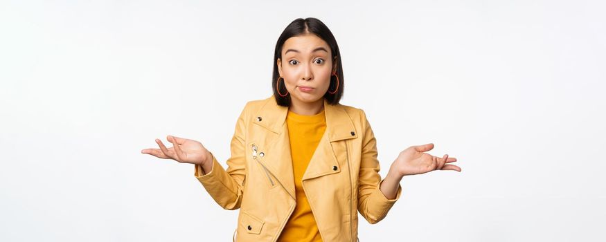 Image of korean girl shrugs shoulders and looks confused, dont know, cant tell, standing over puzzled over white background.