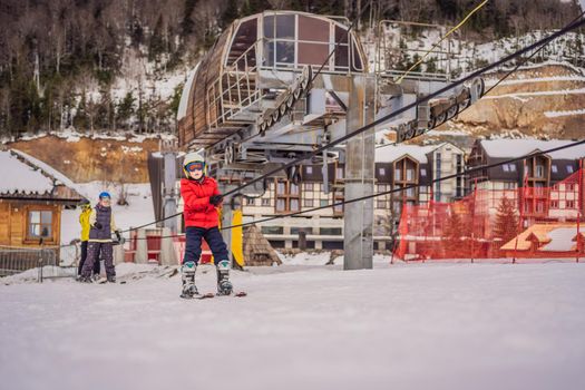 Boy uses a training lift. Child skiing in mountains. Active toddler kid with safety helmet, goggles and poles. Ski race for young children. Winter sport for family. Kids ski lesson in alpine school. Little skier racing in snow.