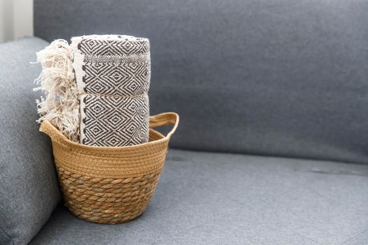 Tweed plaid rolled up in a wicker basket on a gray sofa