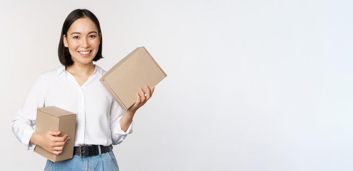 Concept of shopping and delivery. Young happy asian woman posing with boxes and smiling, standing over white background.