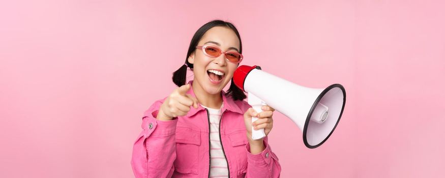 Attention, announcement concept. Enthusiastic asian girl shouting in megaphone, advertising with speaker, recruiting, standing over pink background.