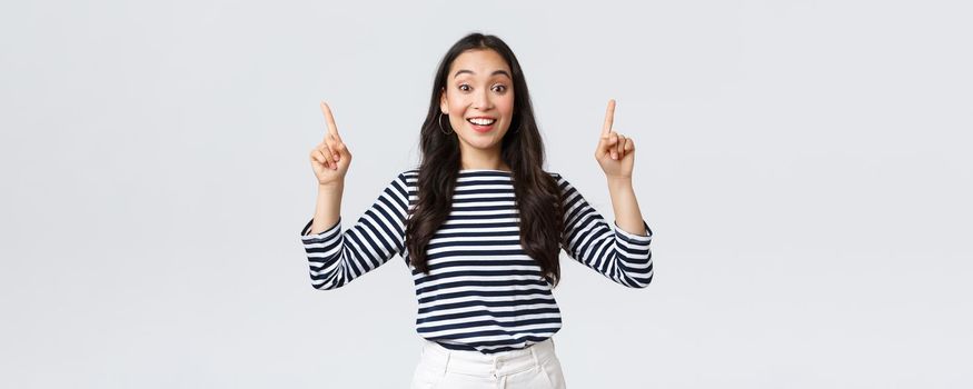 Lifestyle, beauty and fashion, people emotions concept. Amazed rejoicing asian female customer found excellent price discount, pointing fingers up at top promo and smiling amused.