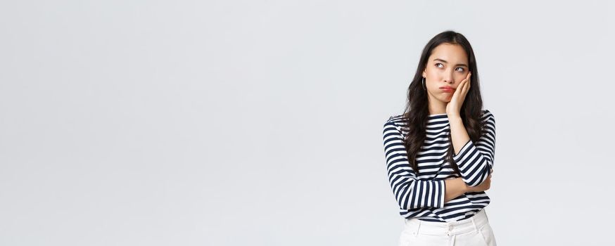Lifestyle, people emotions and casual concept. Annoyed reluctant asian woman standing bored and disappointed at party, lean on palm and looking up irritated, white background.