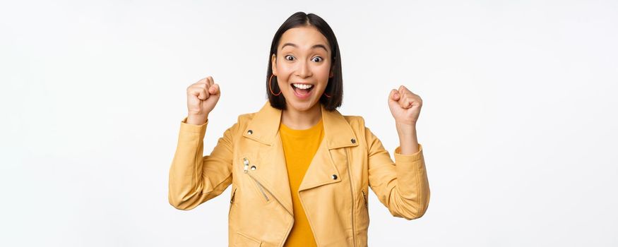Image of asian woman dancing and smiling happy, celebrating victory, triumphing, standing over white background. copy space