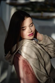 portrait of beautiful gentle woman in a beige sports jacket in the sunshine. Black long hair. sensuality and tenderness. Big red lips