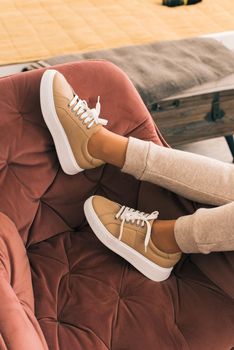 photo of a women legs in beige sports suit and stylish leather sneakers posing in the chair. selective focus. Indoors