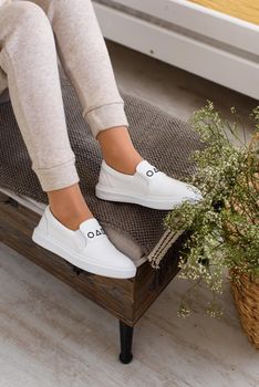 photo of a womens legs in beige sports suit and stylish white leather sneakers posing on a bench. selective focus. Indoors