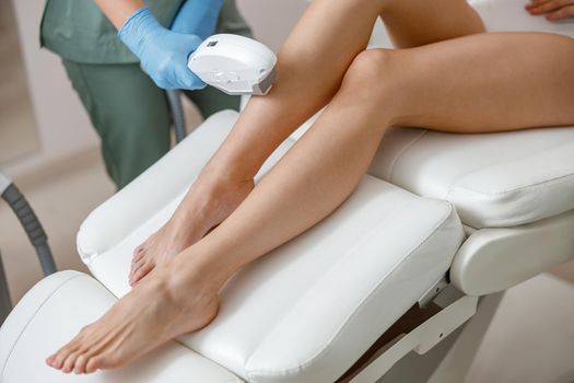 Smooth skin of legs. Photo epilation procedure in beauty salon. Woman in underwear sitting on daybed