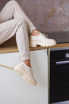 Part photo of a women in beige sports suit and stylish leather oxfords shoes posing on the kitchen. Indoors