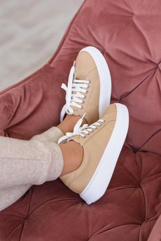 photo of a women legs in beige sports suit and stylish leather sneakers posing in the chair. selective focus. Indoors