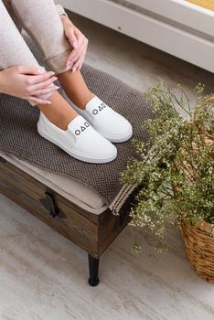 photo of a womens legs in beige sports suit and stylish white leather sneakers posing on a bench. selective focus. Indoors