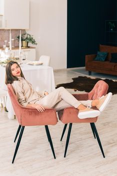photo of a women in beige sports suit and stylish leather sneakers posing in the chair on a kitchen . selective focus. Indoors