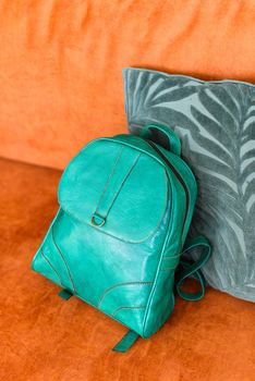 A green leather modern backpack on a orange sofa. Indoors