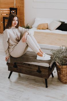 photo of a women in beige sports suit and stylish white leather sneakers posing on a bench. selective focus. Indoors