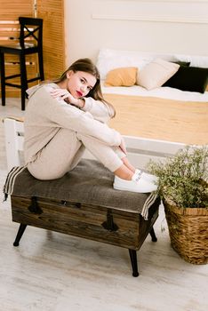 photo of a women in beige sports suit and stylish white leather sneakers posing on a bench. selective focus. Indoors