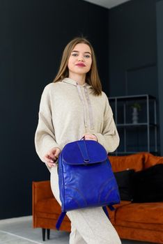 photo of a women in beige sports suit and blue leather backpack posing in a hotel room. selective focus. Indoors